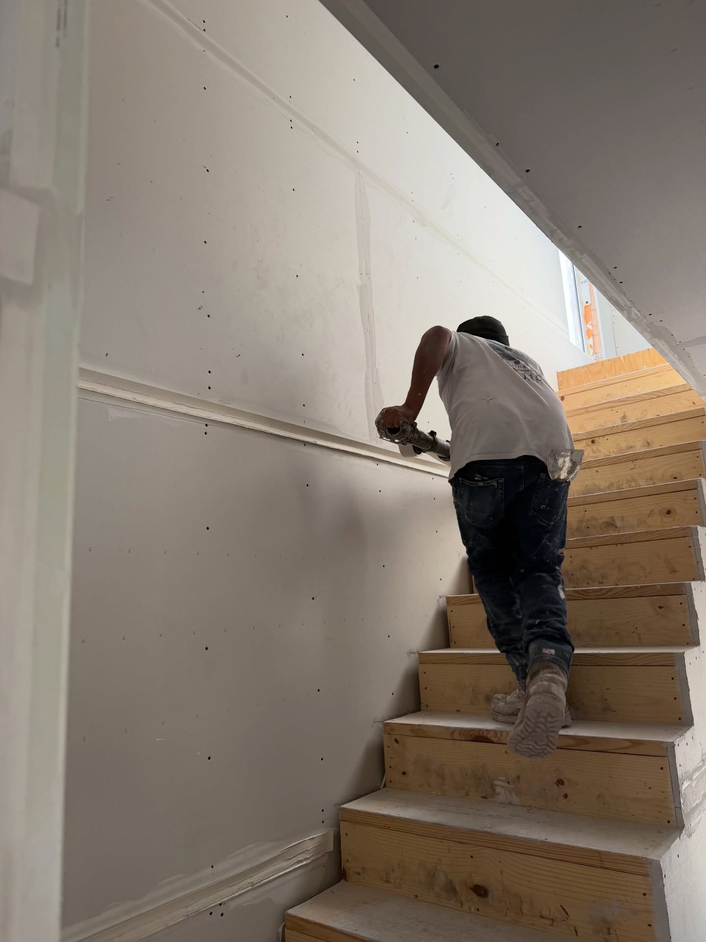 Worker screwing drywall boards on stairway framing